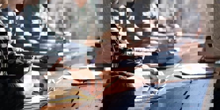 En række mennesker sidder med armene lænet ind over et brunt plankebord fra to sider