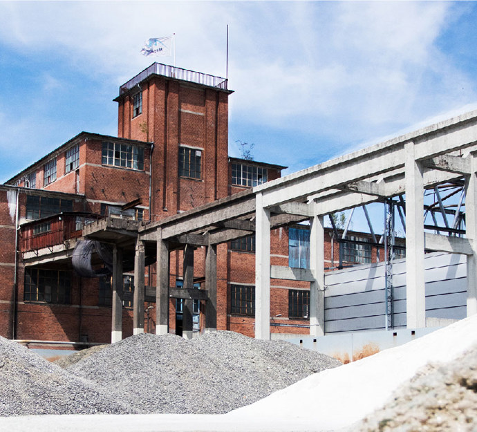 Gamle, rødstensfabriksbygninger på Maglemølle i Næstved med bjerge af knust, hvidt glas i forgrunden. Dette er en del af udendørsarealet hos Reiling Glasrecycling