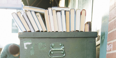 Ovenpå en stor, grøn metalbeholder står en række af bøger med bunden vendt ud mod beskueren