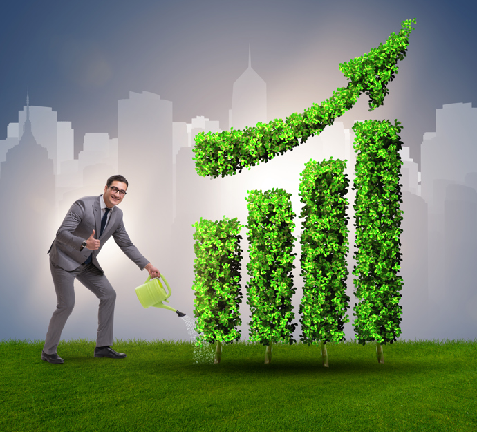 Mand i grå habit vander med vandkande på en opadgående kurve lavet af grønt græs, mens han vender tommelfingeren op til fotografen